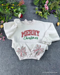 Flat lay of a white crewneck sweatshirt embroidered with red plaid Merry Christmas chest text and festive bow sleeve detail
