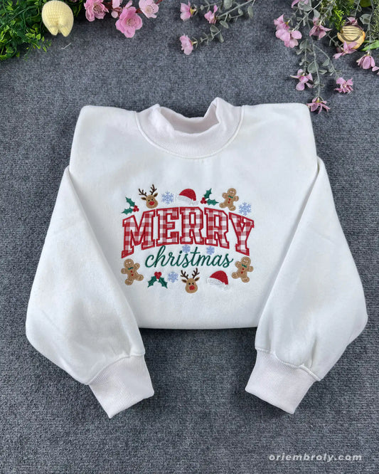 Flat lay of a white crewneck sweatshirt embroidered with red plaid Merry Christmas text and festive icons like reindeer and gingerbread