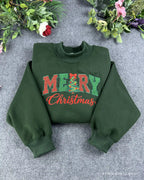 Flat lay of a forest green crewneck sweatshirt embroidered with red Merry Christmas text featuring a Christmas tree letter design