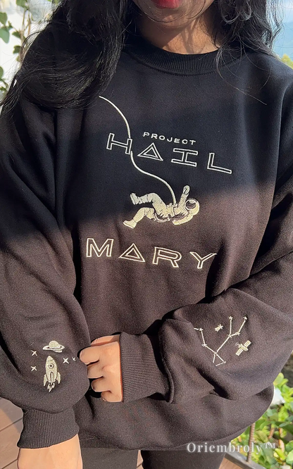 Minimalist sci-fi streetwear: black crewneck with detailed astronaut and cosmic sleeve embroidery. Narrative-driven apparel inspired by modern literature and outer space exploration, perfect for a clean, aesthetic look