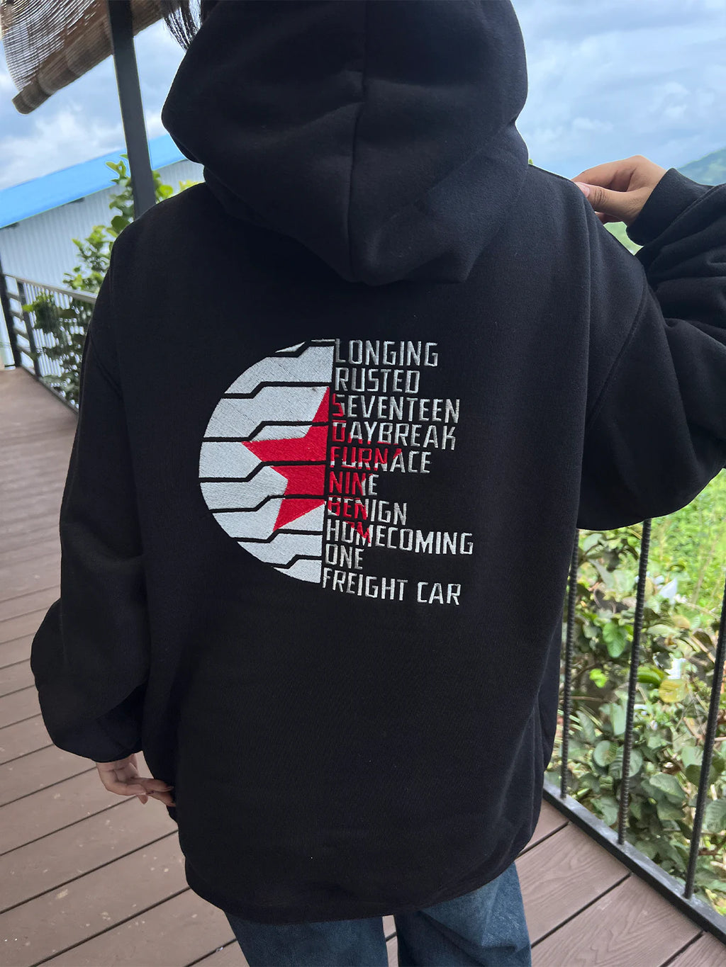 Black hoodie with text and graphic design on the back, worn by a person outdoors.