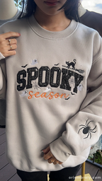 Model wearing sand beige spooky season embroidered crewneck jumper showing custom embroidered spider on sleeve.