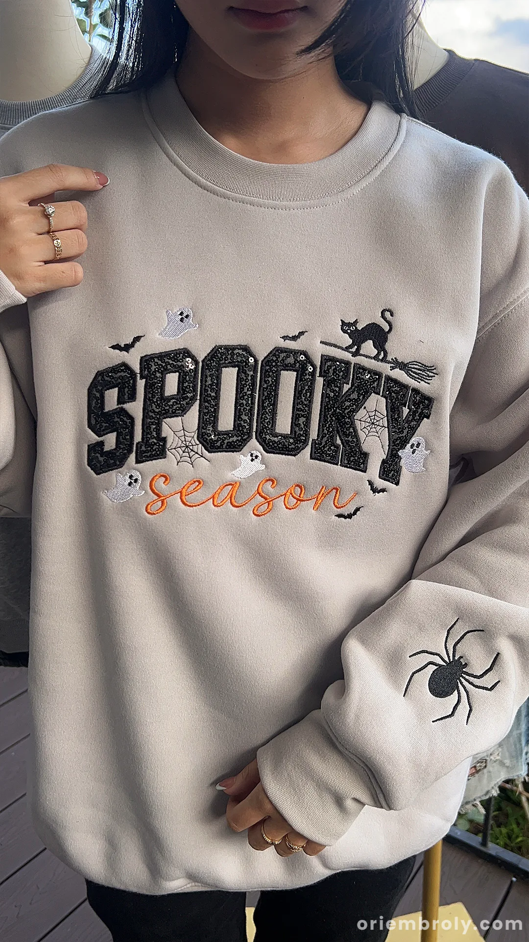 Model wearing sand beige spooky season embroidered crewneck jumper showing custom embroidered spider on sleeve.