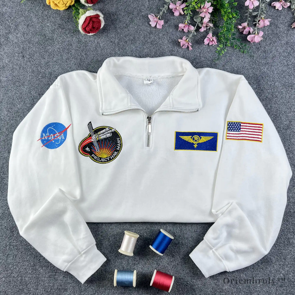Premium white quarter-zip sweatshirt with authentic NASA meatball logo and astronaut flight patches. High-quality embroidery for space enthusiasts and STEM students