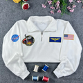 Premium white quarter-zip sweatshirt with authentic NASA meatball logo and astronaut flight patches. High-quality embroidery for space enthusiasts and STEM students
