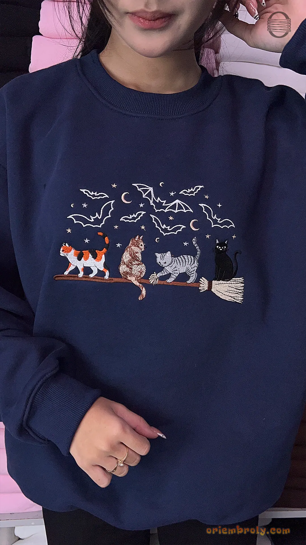 Model wearing a navy blue Halloween crewneck sweater embroidered with cats riding a magic broomstick