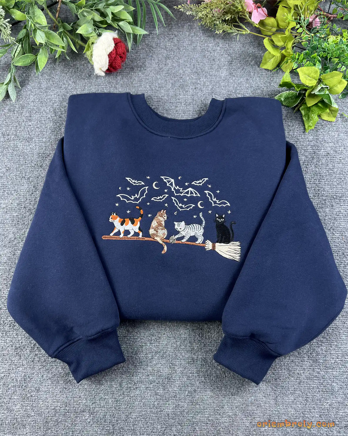 Flat lay of a navy blue Halloween embroidered crewneck sweatshirt featuring witchy broomstick cats and bats