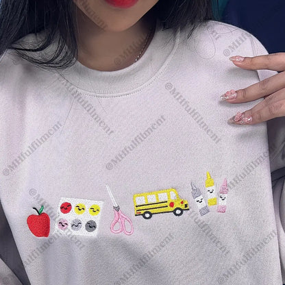 White sweatshirt with various embroidered designs including an apple, scissors, a school bus, and more.