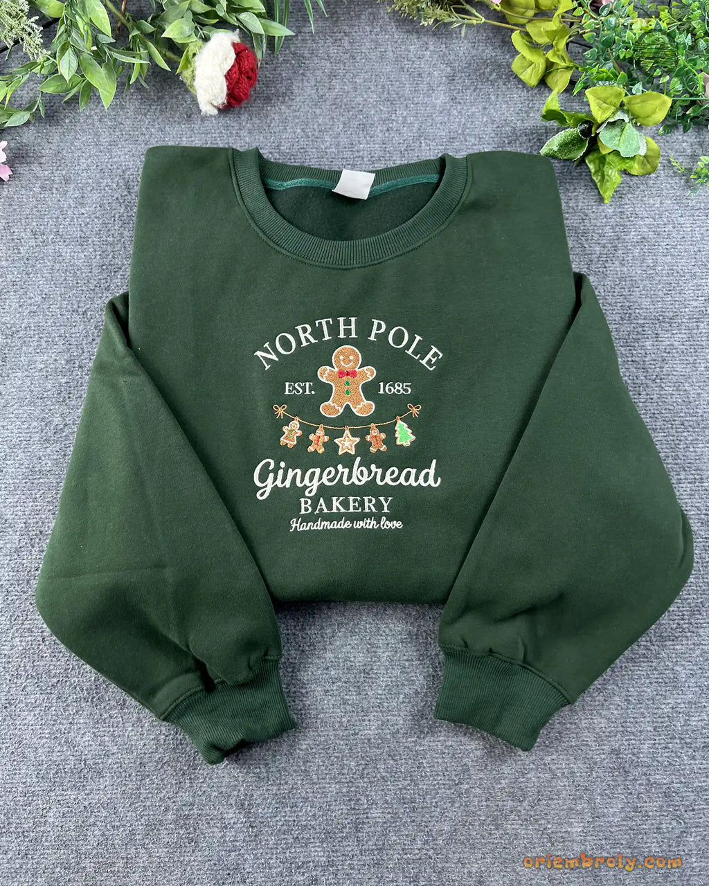 Flat lay of a forest green Christmas crewneck sweatshirt embroidered with North Pole Gingerbread Bakery and gingerbread man