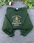 Flat lay of a forest green Christmas crewneck sweatshirt embroidered with North Pole Gingerbread Bakery and gingerbread man