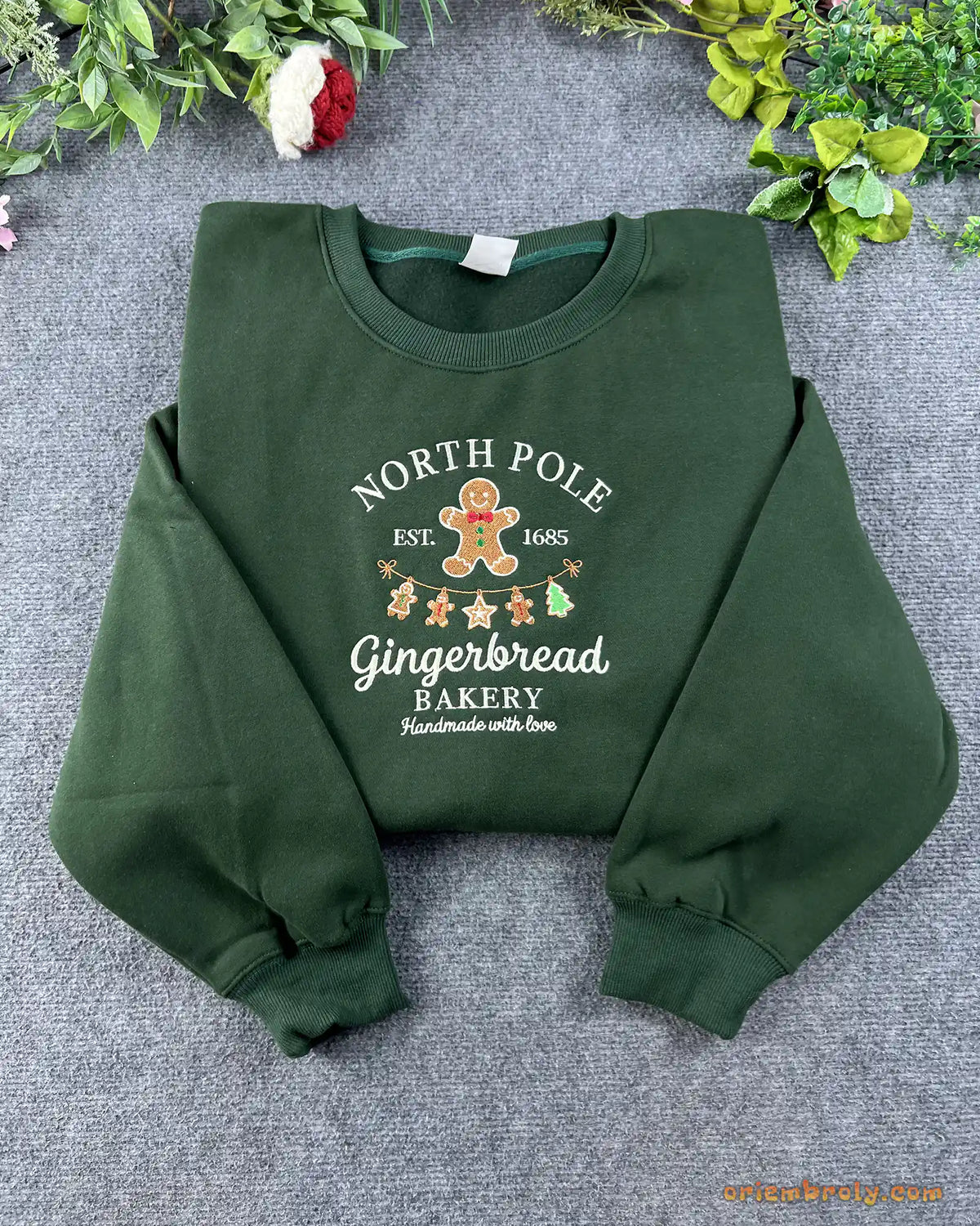 Flat lay of a forest green Christmas crewneck sweatshirt embroidered with North Pole Gingerbread Bakery and gingerbread man