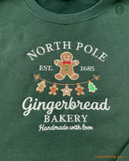 Close-up of North Pole Gingerbread Bakery embroidery featuring a cute gingerbread man, Christmas trees, and stars on a green sweater