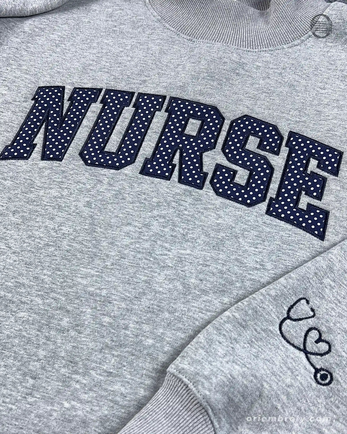 Close-up of textured dark varsity nurse chest embroidery and cute stethoscope with heart line embroidered on the sleeve of a grey sweater
