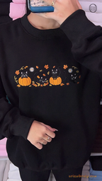Model wearing an oversized black embroidered crewneck sweater with black cats in pumpkins design for spooky season