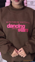 Model wearing an oversized chocolate brown I'd Rather Be Watching Dancing with the Stars embroidered crewneck sweater