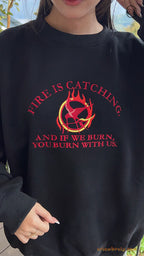 Model wearing an oversized black Fire Is Catching embroidered crewneck sweater for Hunger Games bookish outfit