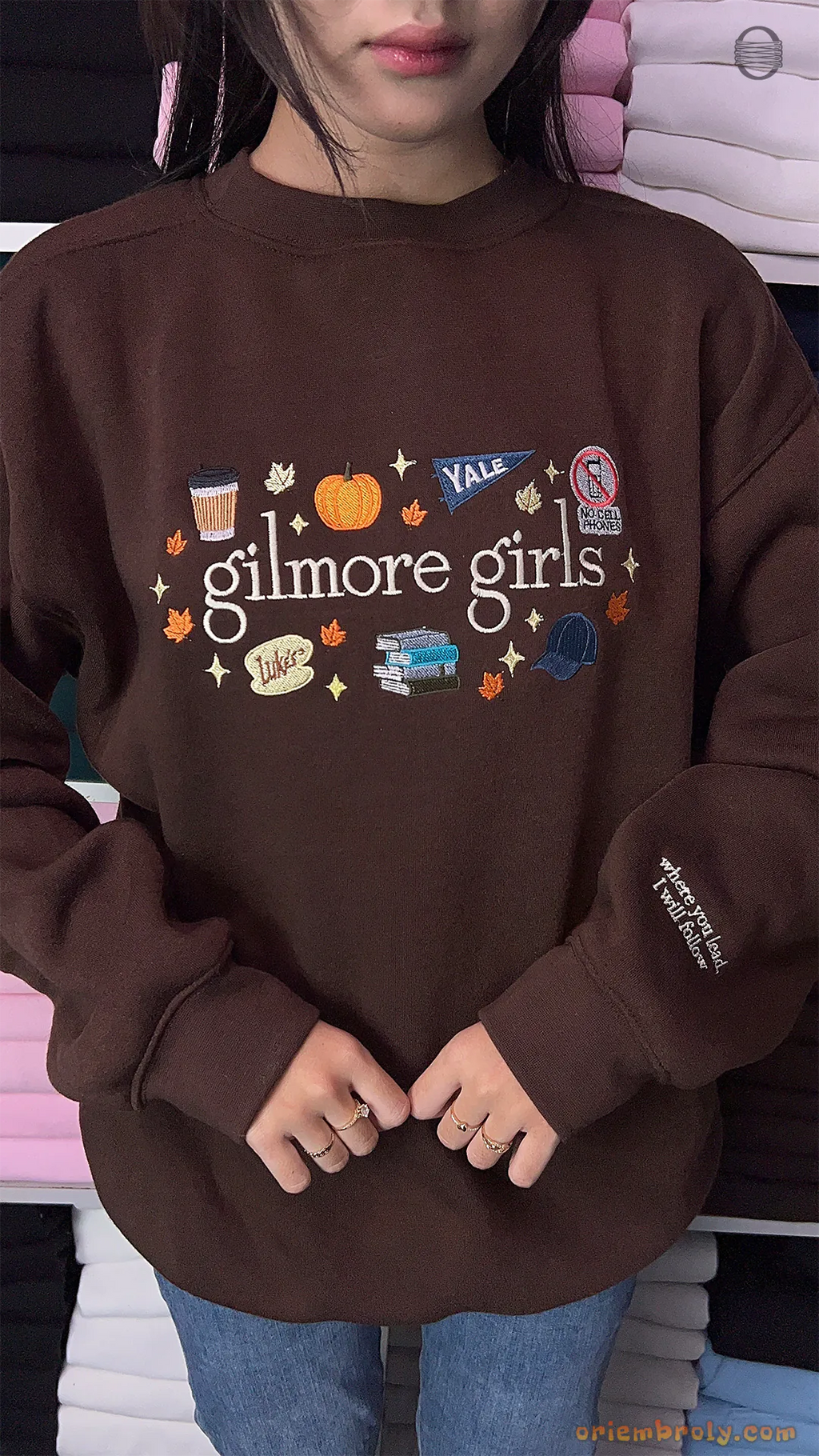 Model wearing an oversized brown Gilmore Girls embroidered sweatshirt paired with blue jeans