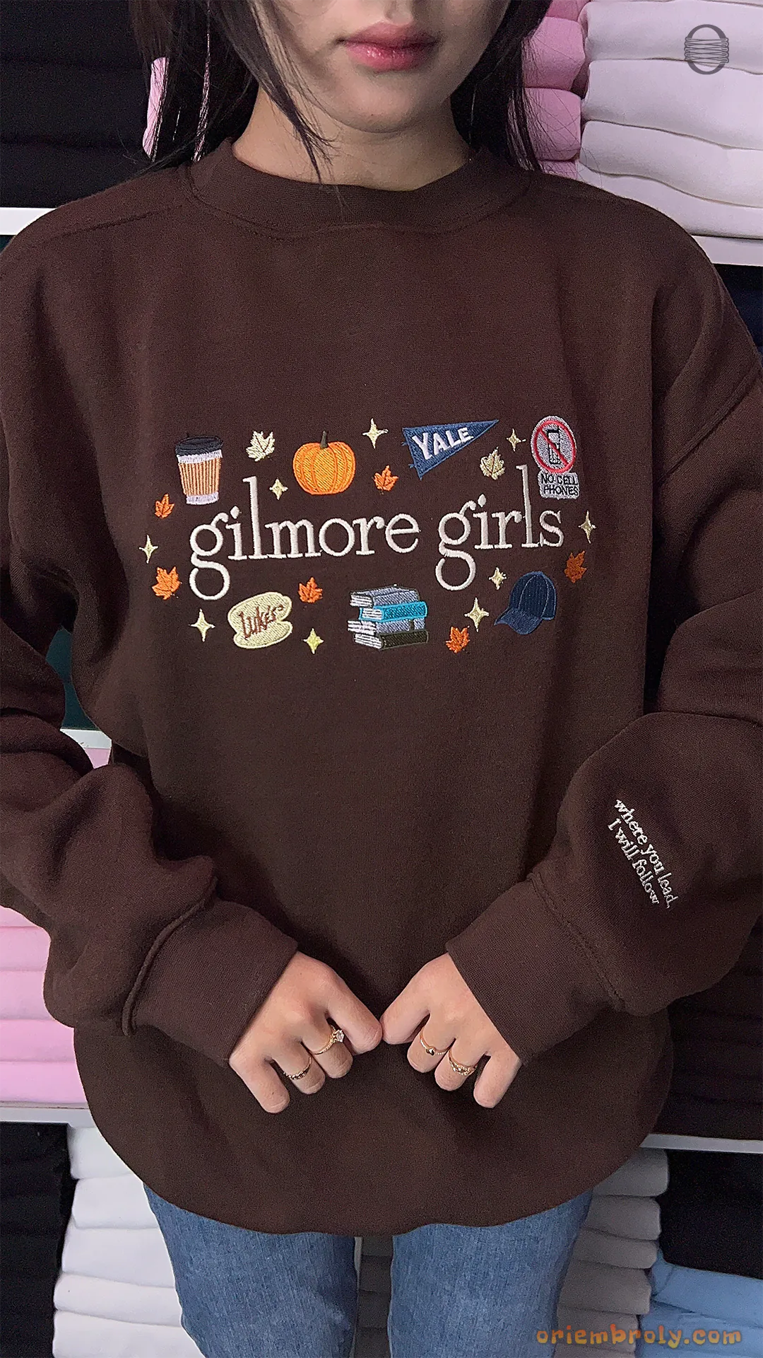 Model wearing an oversized brown Gilmore Girls embroidered sweatshirt paired with blue jeans