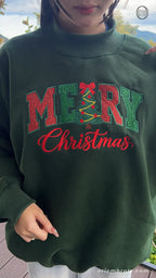 Model wearing an oversized forest green Merry Christmas embroidered crewneck sweater outdoors for holiday outfit
