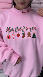 Model wearing an oversized light pink Christmas ornaments garland embroidered crewneck sweater with red Merry Christmas collar detail
