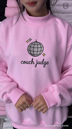 Model wearing an oversized light pink Couch Judge embroidered crewneck sweater for reality tv show watch party outfit