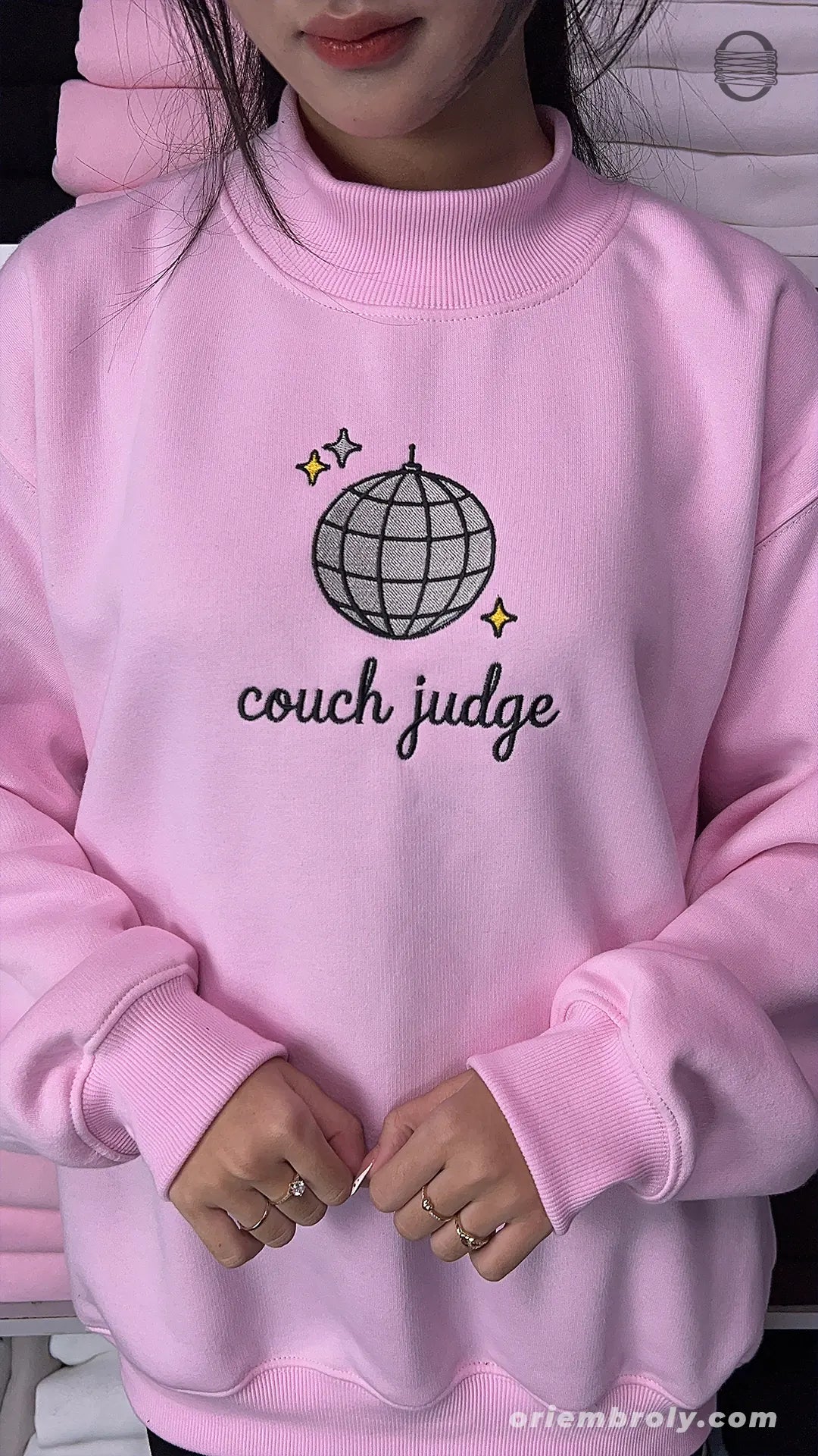 Model wearing an oversized light pink Couch Judge embroidered crewneck sweater for reality tv show watch party outfit