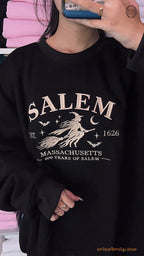 Model wearing an oversized black Salem Massachusetts flying witch embroidered crewneck sweater for Halloween outfit