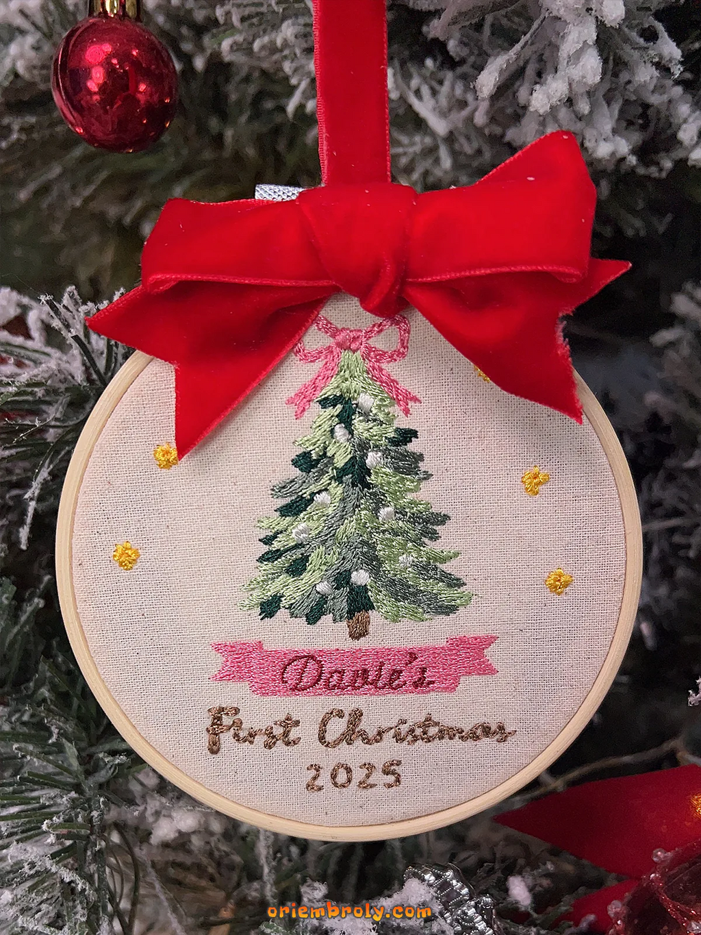 Embroidered ornament with a Christmas tree design and red bow on a Christmas tree.