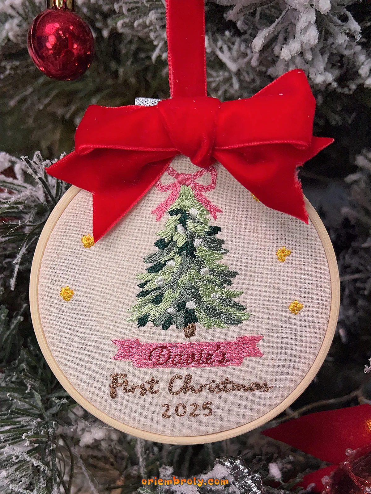 Embroidered ornament with a Christmas tree design and red bow on a Christmas tree.