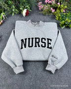 Flat lay of a sport grey sweatshirt embroidered with black varsity nurse block letters and custom name sleeve detail