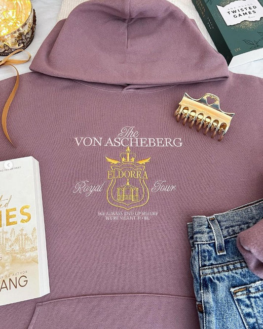 A purple hooded sweatshirt with 'The Von Ascheberg' embroidered on the front, displayed with a book and jeans.