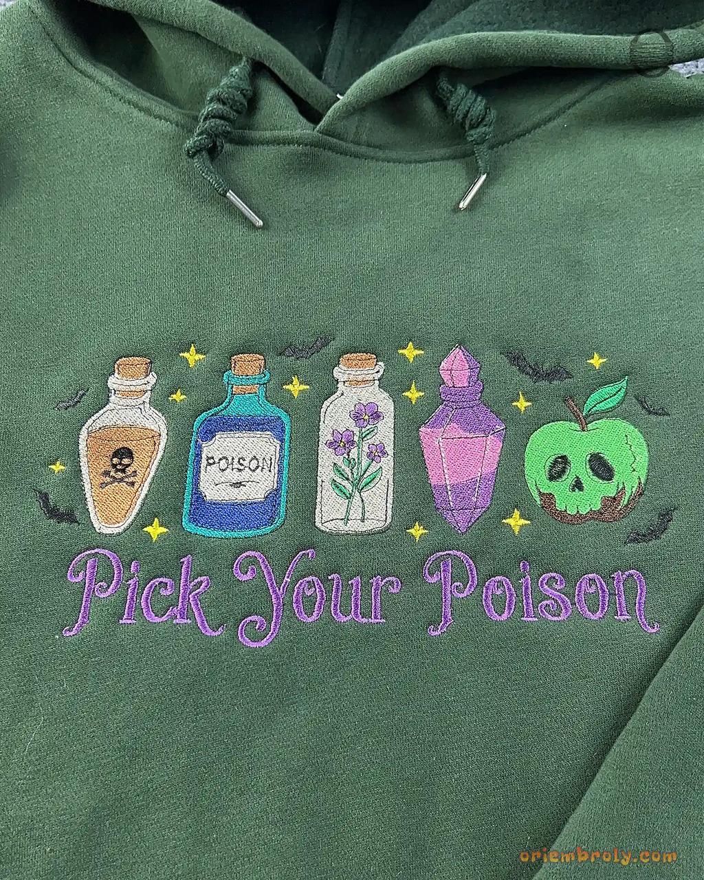 Close-up of Pick Your Poison purple text and colorful potion bottles embroidery on a forest green hoodie