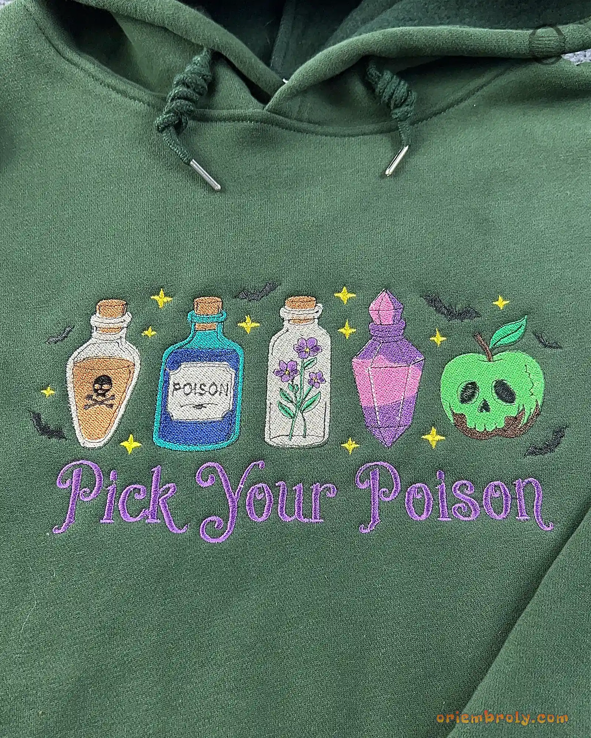Close-up of Pick Your Poison purple text and colorful potion bottles embroidery on a forest green hoodie
