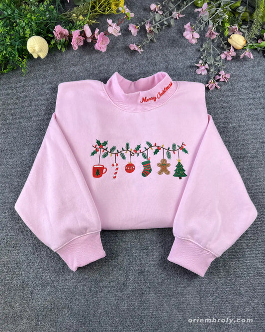 Flat lay of a light pink crewneck sweatshirt embroidered with Christmas ornaments garland and red Merry Christmas collar embroidery