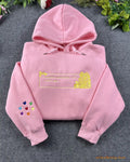 Flat lay of a light pink hoodie embroidered with gold romantic hearts quote and colorful rainbow hearts on sleeve