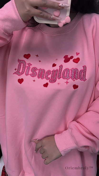 Soft pastel pink sweatshirt with glitter embroidery, perfect for theme park fans and anyone who loves a little magic.