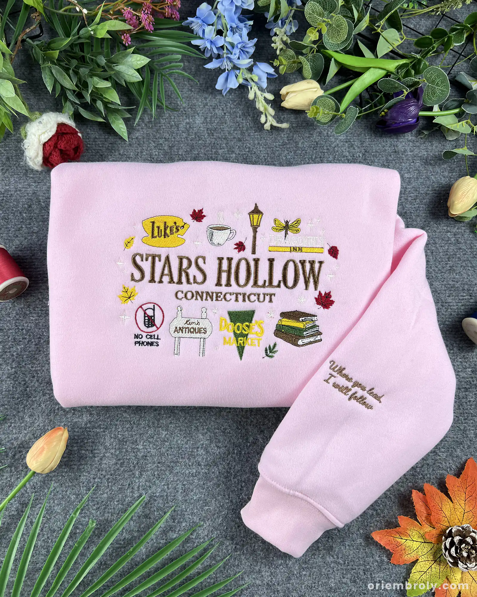 Folded baby pink crewneck sweatshirt embroidered with Stars Hollow Connecticut text, autumn icons, and custom sleeve embroidery quote.