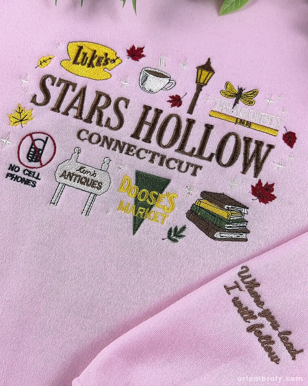 Close-up of pink Stars Hollow Connecticut embroidery featuring Luke's sign, coffee cup, gazebo graphics, and embroidered quote on the sleeve cuff.