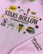 Close-up of pink Stars Hollow Connecticut embroidery featuring Luke's sign, coffee cup, gazebo graphics, and embroidered quote on the sleeve cuff.