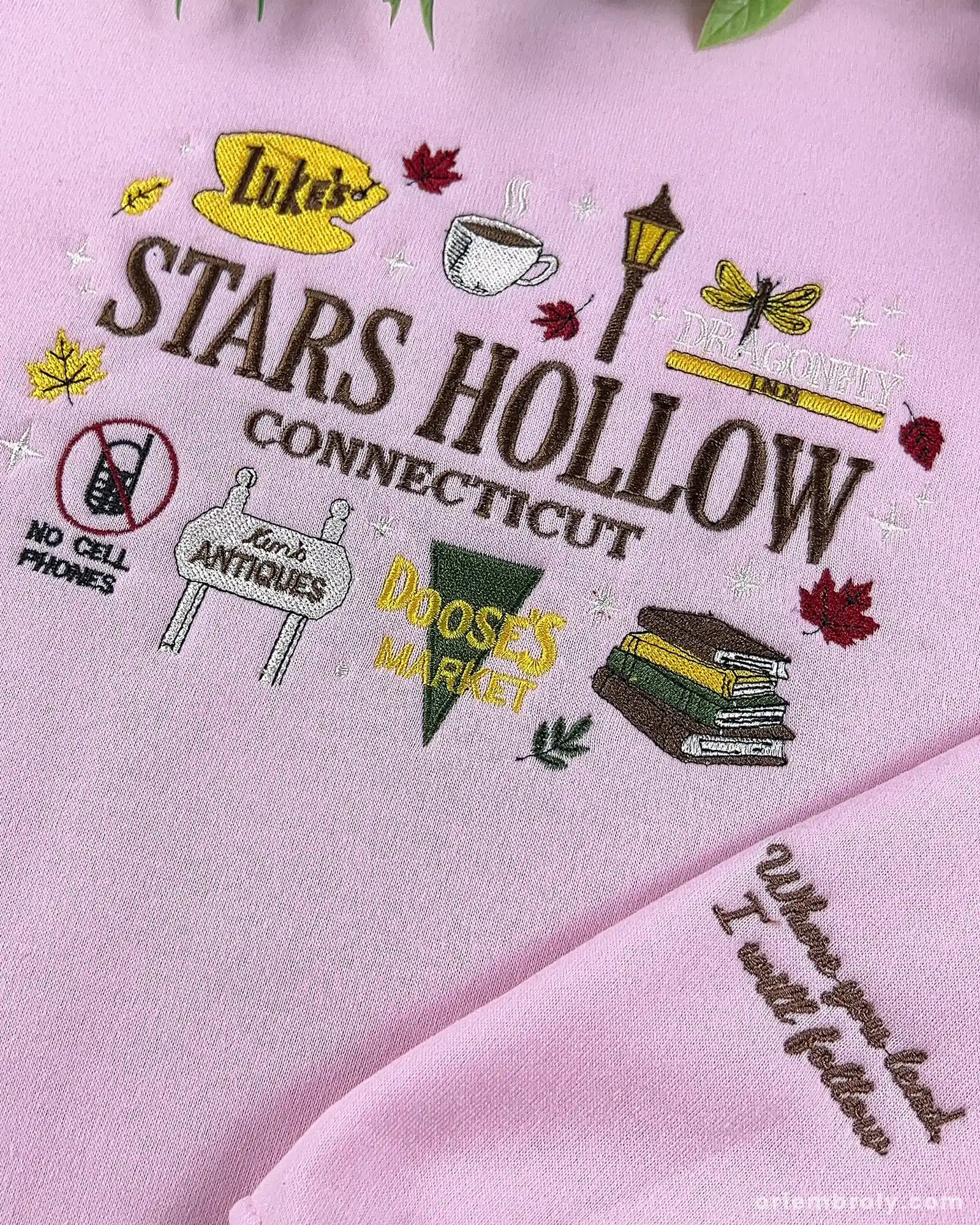 Close-up of pink Stars Hollow Connecticut embroidery featuring Luke's sign, coffee cup, gazebo graphics, and embroidered quote on the sleeve cuff.