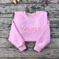 Pink embroidered sweatshirt featuring cat, dog, syringe, stethoscope, and heart designs — perfect for veterinarians or pet lovers.