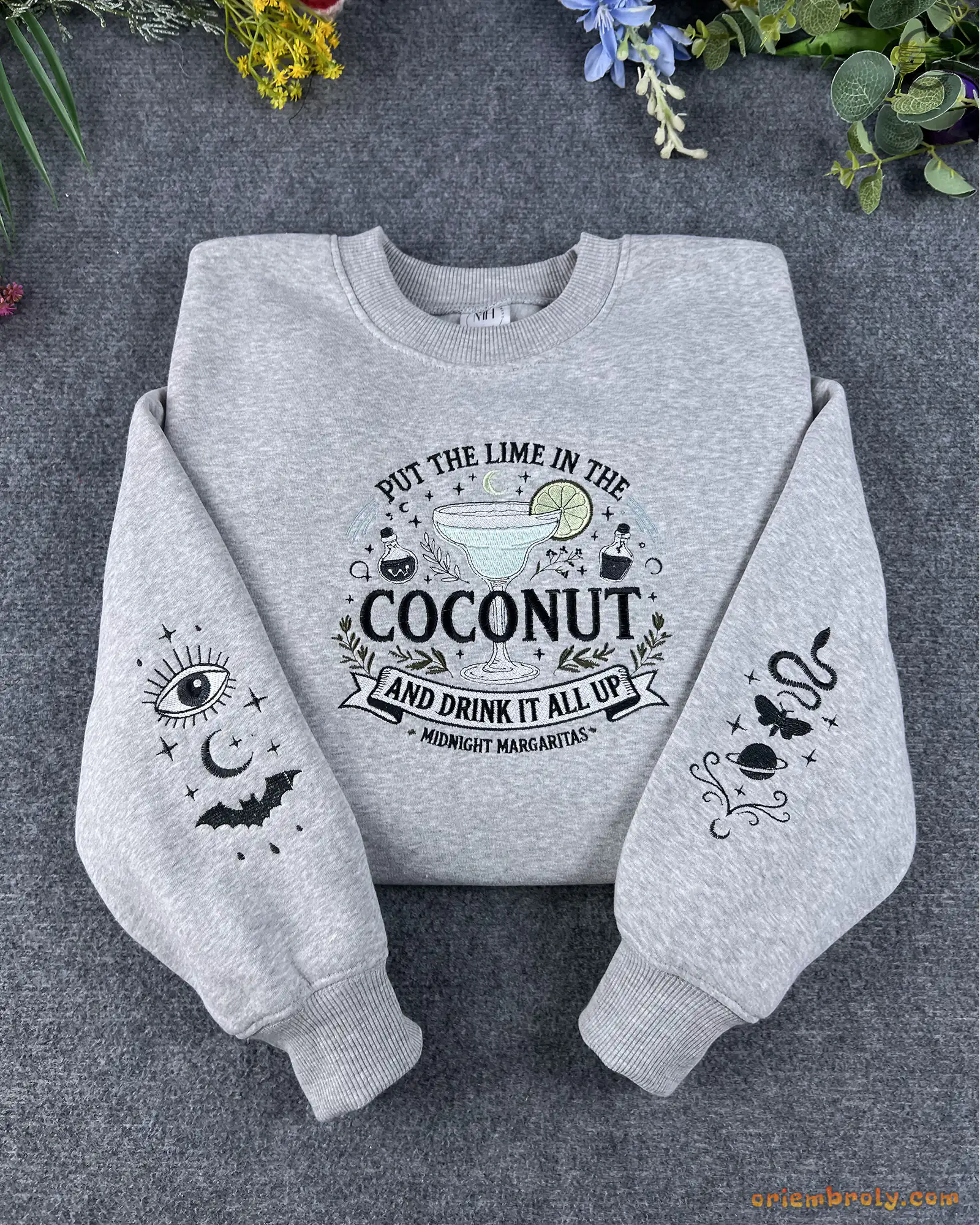 Flat lay of a grey Practical Magic embroidered sweatshirt with Put The Lime In The Coconut text and spooky sleeve embroidery