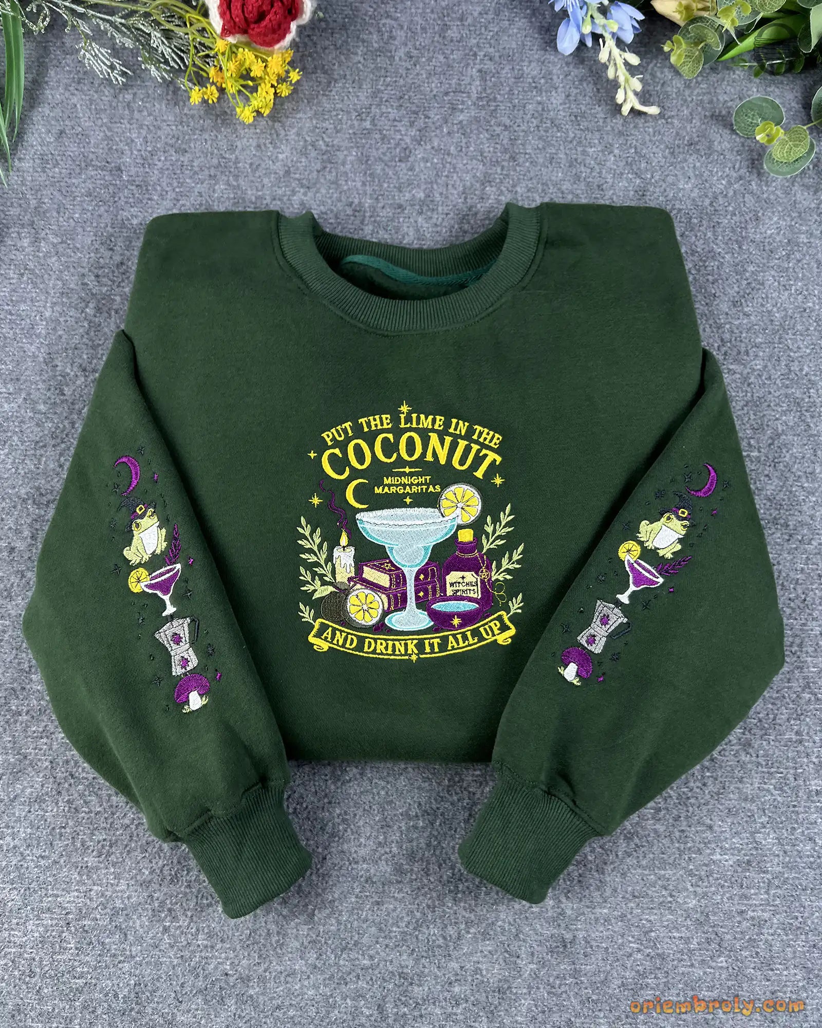 Flat lay of a forest green Practical Magic embroidered sweatshirt featuring witchy frog and cocktail sleeve details