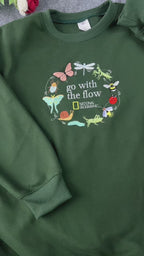 Video showing embroidered details of Go With The Flow nature insects design on a forest green sweatshirt