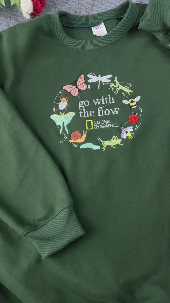 Video showing embroidered details of Go With The Flow nature insects design on a forest green sweatshirt