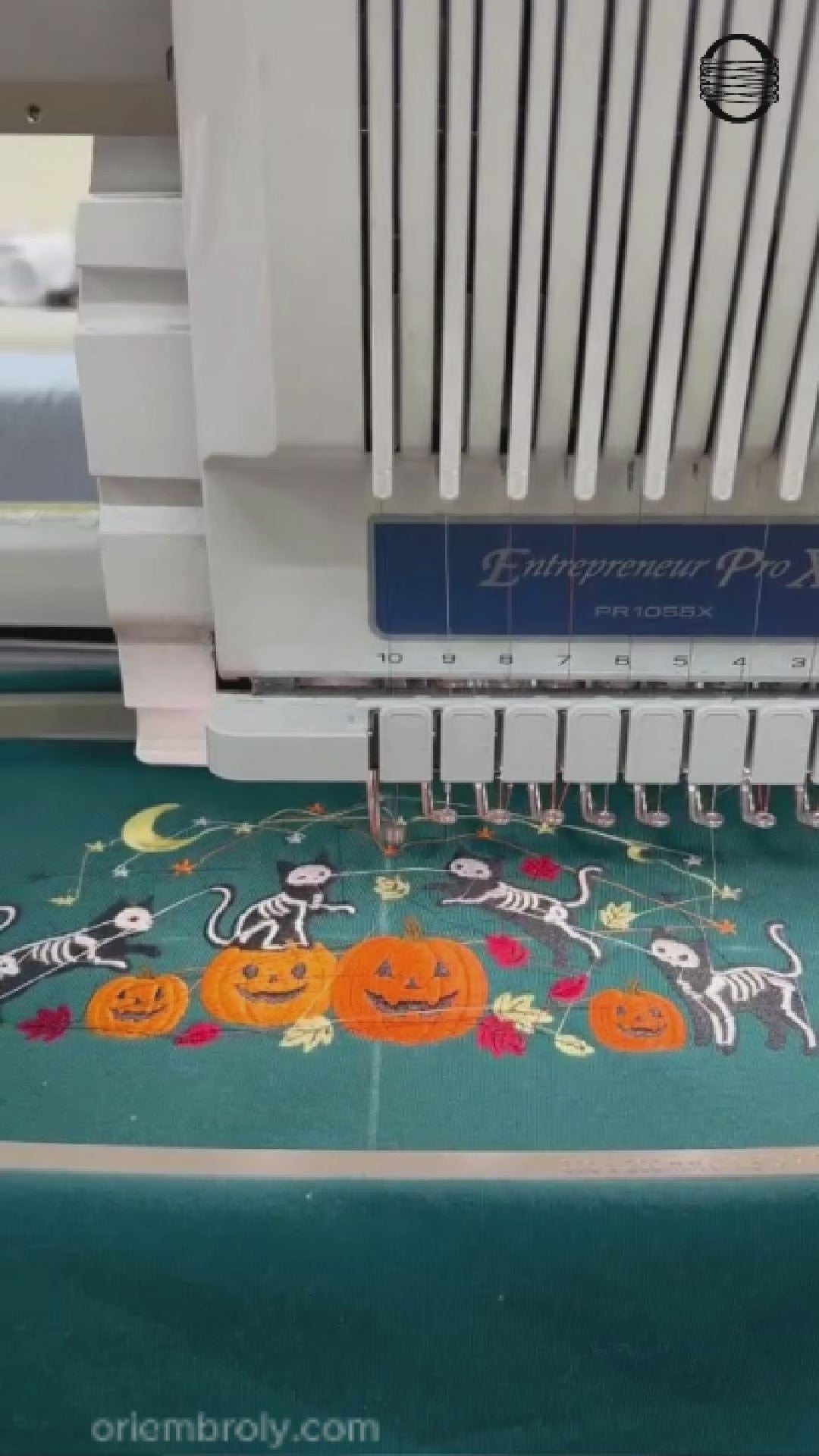 Video showing a computer embroidery machine stitching skeleton cats and pumpkin design on a teal sweatshirt.