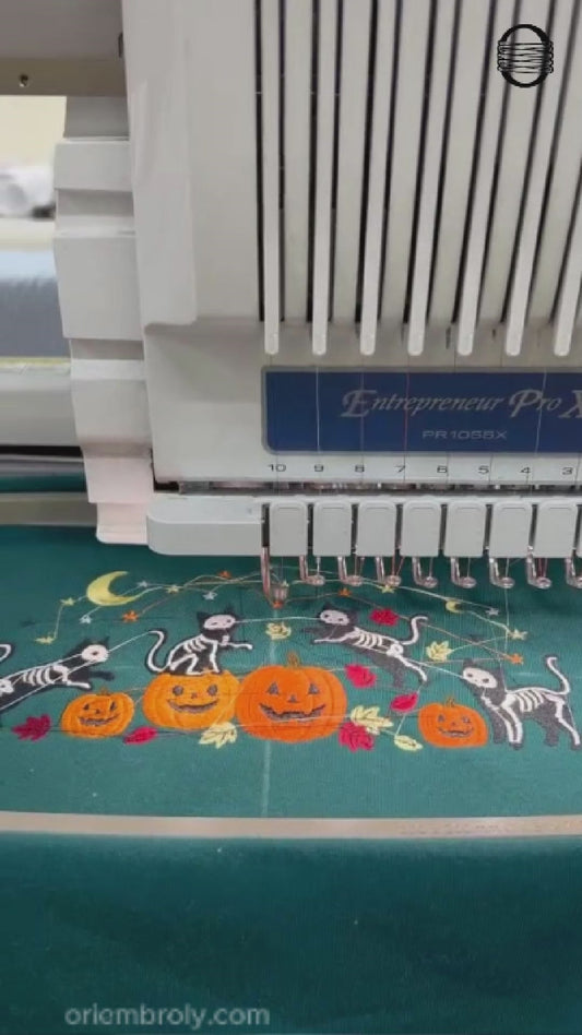 Video showing a computer embroidery machine stitching skeleton cats and pumpkin design on a teal sweatshirt.