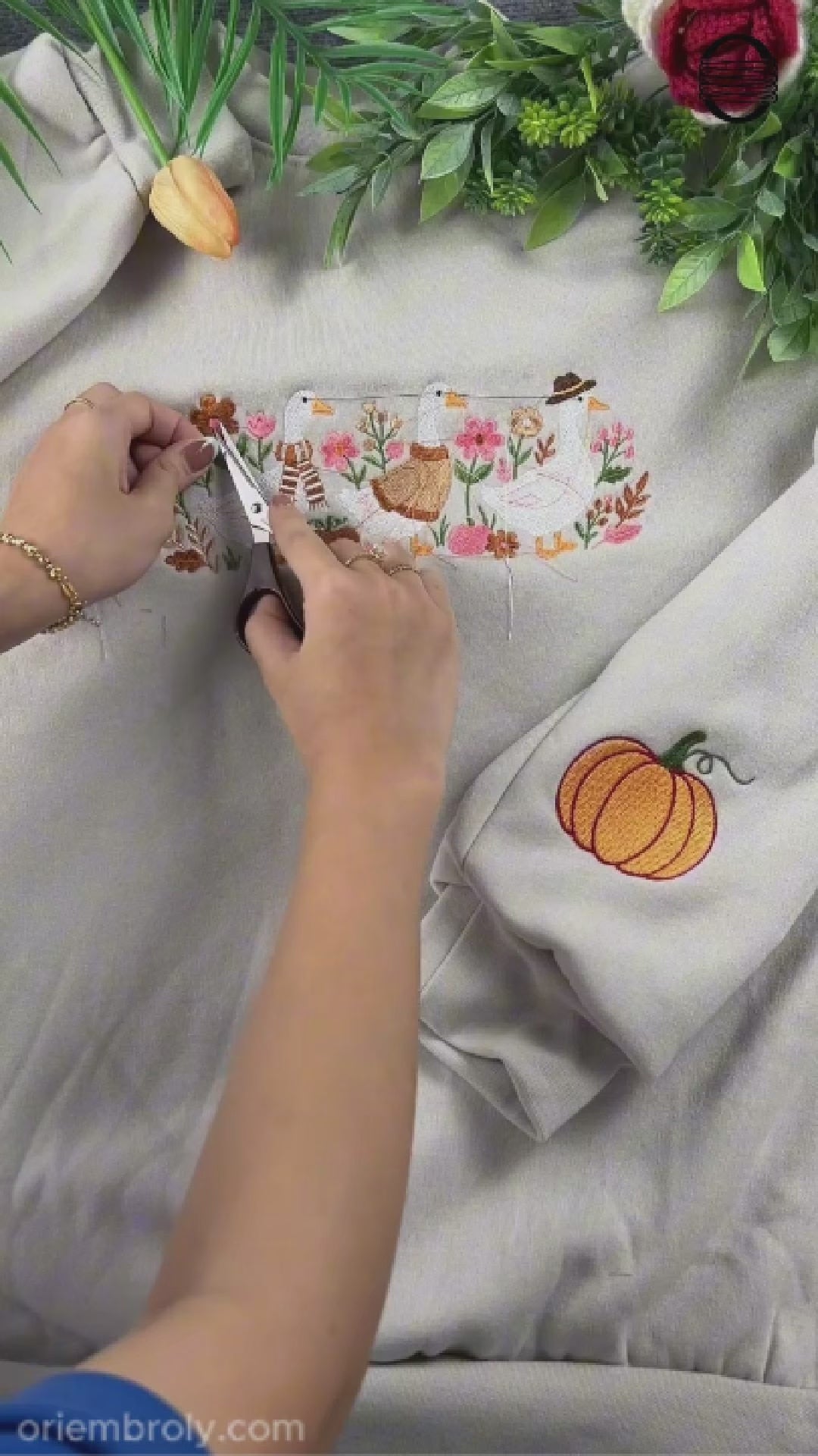 Close-up video of hands using small embroidery scissors to cut loose threads on a custom embroidered sweatshirt.