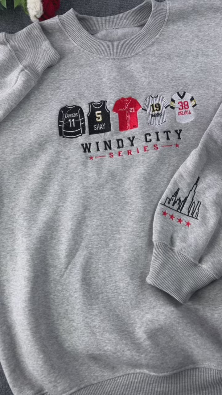 Video showing embroidered details of Chicago sports jerseys and city skyline on a heather grey crewneck sweater