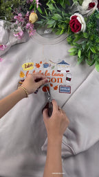 Hands using small embroidery scissors to cut loose threads on a custom La La La Season embroidered sweatshirt.